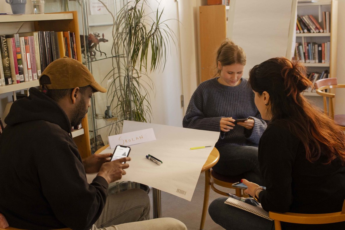 Tre personer sitter runt ett bord och diskuterar.