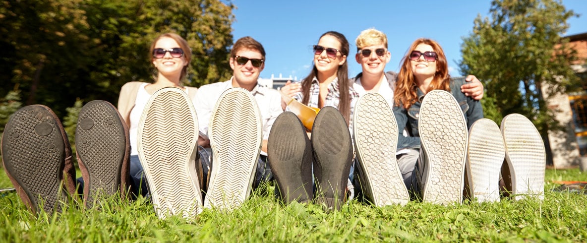 Fem unga personer sitter på en gräsmatta med skosulorna riktade mot kameran.